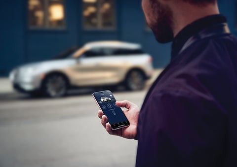 A person is shown interacting with a smartphone to connect to a Lincoln vehicle across the street. | Irwin Lincoln in Freehold NJ